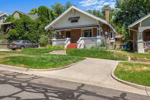 Bungalow-style house featuring covered porch, a chimney, a front lawn, and brick siding