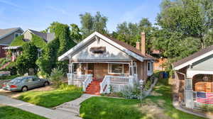 Bungalow-style home with a chimney, covered porch, a front yard, and brick siding