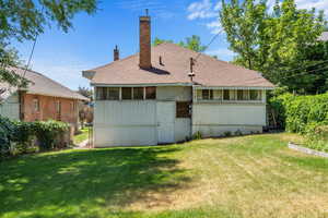 Rear view of property featuring a sunroom, a chimney, and a shingled roof