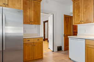 Kitchen featuring freestanding refrigerator, dishwasher, light countertops, and brown cabinetry