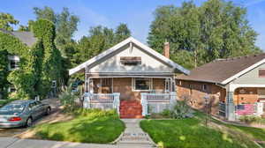 Bungalow featuring a front lawn, brick siding, a chimney, and a porch