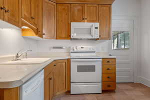 Kitchen with white appliances, brown cabinetry, and light countertops