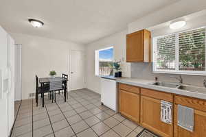 Kitchen featuring light countertops, a textured ceiling, white appliances, light tile patterned floors, and brown cabinets