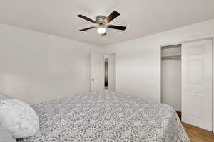 Bedroom featuring a textured ceiling, a ceiling fan, a closet, and wood finished floors