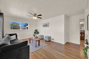 Living room with light wood-style flooring, a textured ceiling, healthy amount of natural light, and a ceiling fan