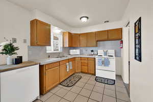 Kitchen featuring white appliances, a textured ceiling, light tile patterned floors, and brown cabinetry