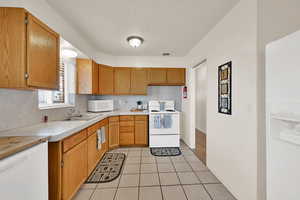 Kitchen featuring light countertops, white appliances, a textured ceiling, light tile patterned floors, and brown cabinetry