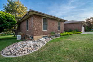 View of property exterior featuring a lawn, a garage, brick siding, and driveway
