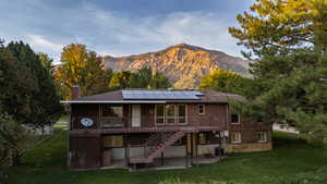 Rear view of house featuring a patio, stairway, a yard, a chimney, and solar panels