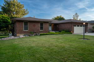Single story home featuring an attached garage, brick siding, a front yard, concrete driveway, and a shingled roof