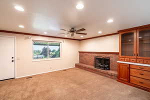 Unfurnished living room with a brick fireplace, crown molding, ceiling fan, recessed lighting, and carpet floors