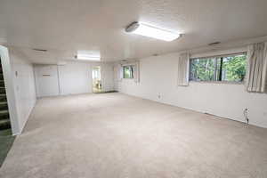 Unfurnished room with a textured ceiling, light colored carpet, and healthy amount of natural light