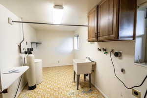 Washroom with electric dryer hookup, a textured ceiling, hookup for a washing machine, cabinet space, and light floors