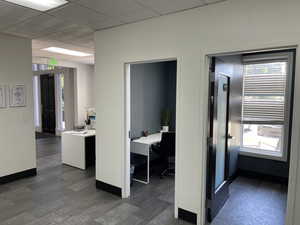Hall with a drop ceiling, an office area, and dark floors