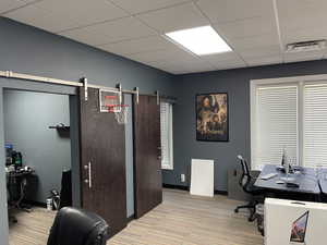 Home office with a barn door, a drop ceiling, and light carpet