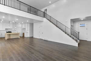 Unfurnished living room with recessed lighting, a high ceiling, dark wood finished floors, and stairway