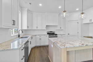 Kitchen with light stone countertops, a kitchen island, dark wood-style flooring, stainless steel appliances, and hanging light fixtures