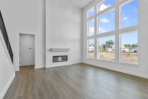 Unfurnished living room with a high ceiling, dark wood-style flooring, a glass covered fireplace, and stairway
