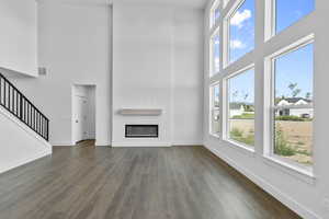 Unfurnished living room featuring a towering ceiling, healthy amount of natural light, dark wood-style floors, and stairway