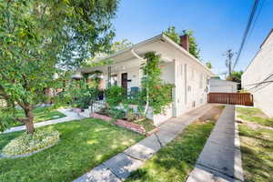 Bungalow with a chimney, a detached garage, covered porch, and a front lawn