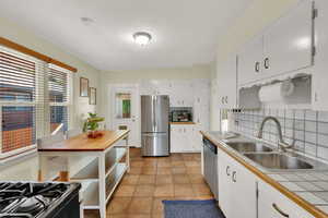 Kitchen featuring stainless steel appliances, decorative backsplash, tile countertops, white cabinetry, and light tile patterned floors, Main Floor