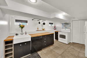 Downstairs Kitchen with white appliances, wood counters, decorative backsplash, light tile patterned floors, and range hood