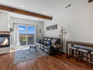 Living area with beam ceiling, a glass covered fireplace, wood finished floors, and recessed lighting