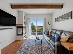 Living room featuring a multi sided fireplace, wood finished floors, recessed lighting, and beamed ceiling