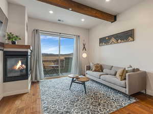 Living room with recessed lighting, beamed ceiling, wood finished floors, and a glass covered fireplace