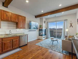 Kitchen featuring beamed ceiling, brown cabinets, light stone counters, dark wood finished floors, and dishwasher