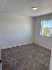 Unfurnished room with dark carpet, a textured ceiling, and a smoke detector