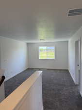 Empty room with dark colored carpet and a textured ceiling