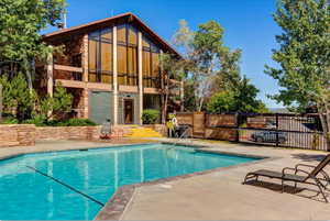 Rear view of property featuring stone siding, a patio area, and a community pool