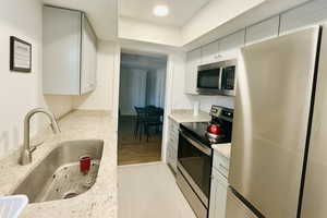Kitchen with appliances with stainless steel finishes, light stone countertops, white cabinetry, and light wood-type flooring