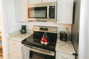 Kitchen with appliances with stainless steel finishes, light stone countertops, and white cabinets