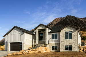 View of front of property with stone siding, board and batten siding, a mountain view, an attached garage, and a shingled roof