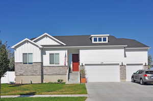 View of front of home with stone siding, board and batten siding, driveway, a front yard, and roof with shingles