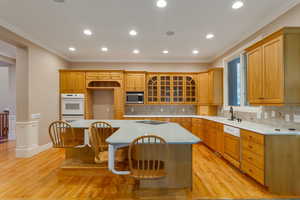 Kitchen featuring crown molding, a breakfast bar area, glass insert cabinets, a center island, and tasteful backsplash