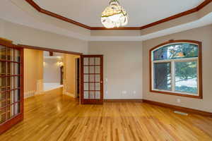 Spare room with ornamental molding, light wood-style flooring, french doors, and a raised ceiling