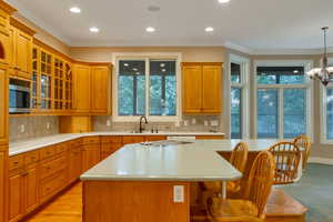 Kitchen with crown molding, a breakfast bar area, tasteful backsplash, a kitchen island with sink, and glass insert cabinets