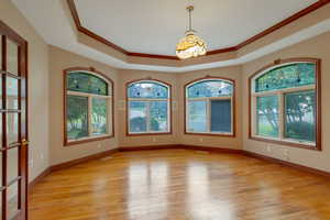 Unfurnished dining area with light wood finished floors, a raised ceiling, crown molding, and french doors