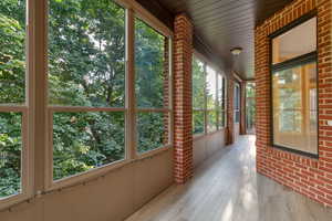 Unfurnished sunroom with brick wall and wood finished floors