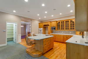 Kitchen featuring tasteful backsplash, glass insert cabinets, recessed lighting, ornamental molding, and light wood-style flooring
