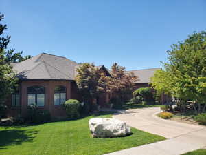 View of front of property featuring a front yard, brick siding, roof with shingles, and curved driveway