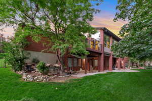 Back of house at dusk with a patio, a lawn, and brick siding