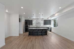 Kitchen with a breakfast bar, a center island with sink, light countertops, light wood-style floors, and decorative backsplash
