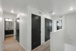 Hallway featuring light colored carpet, recessed lighting, and an upstairs landing