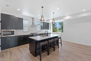 Kitchen featuring dark cabinets, decorative light fixtures, an island with sink, decorative backsplash, and a breakfast bar area