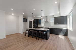 Kitchen featuring a breakfast bar, an island with sink, dark cabinets, tasteful backsplash, and hanging light fixtures