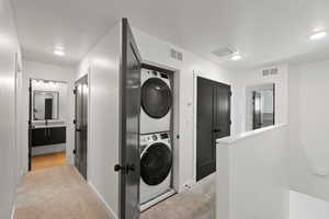 Laundry area with light carpet, stacked washer and clothes dryer, recessed lighting, and a textured ceiling